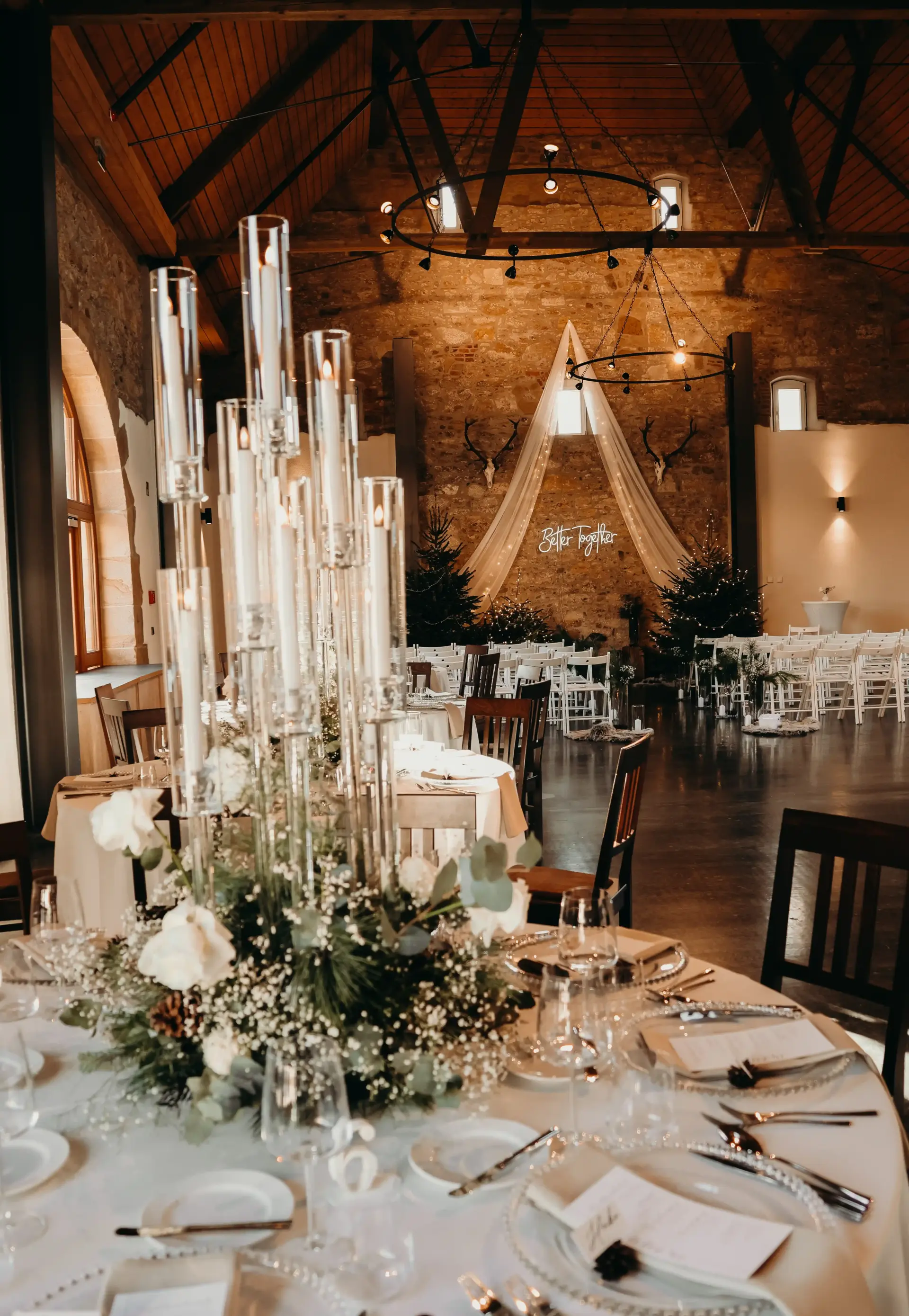 Tischarrangement aus einem gläsernen Kerzenständern mit weißen Kerzen auf einer Winterhochzeit in der Eventscheune.