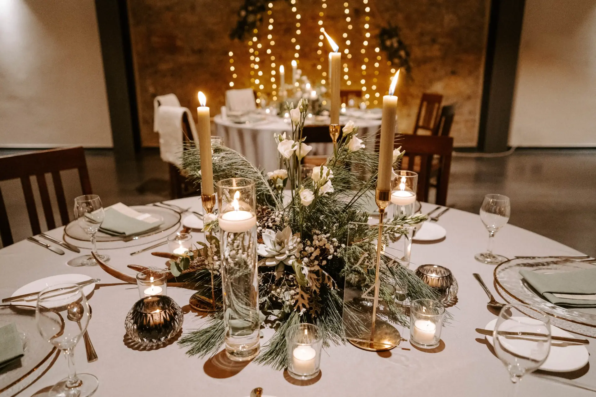 Tischdekoration mit winterlichen Accessoires, weißen Blüten und goldenen Kerzenständern.