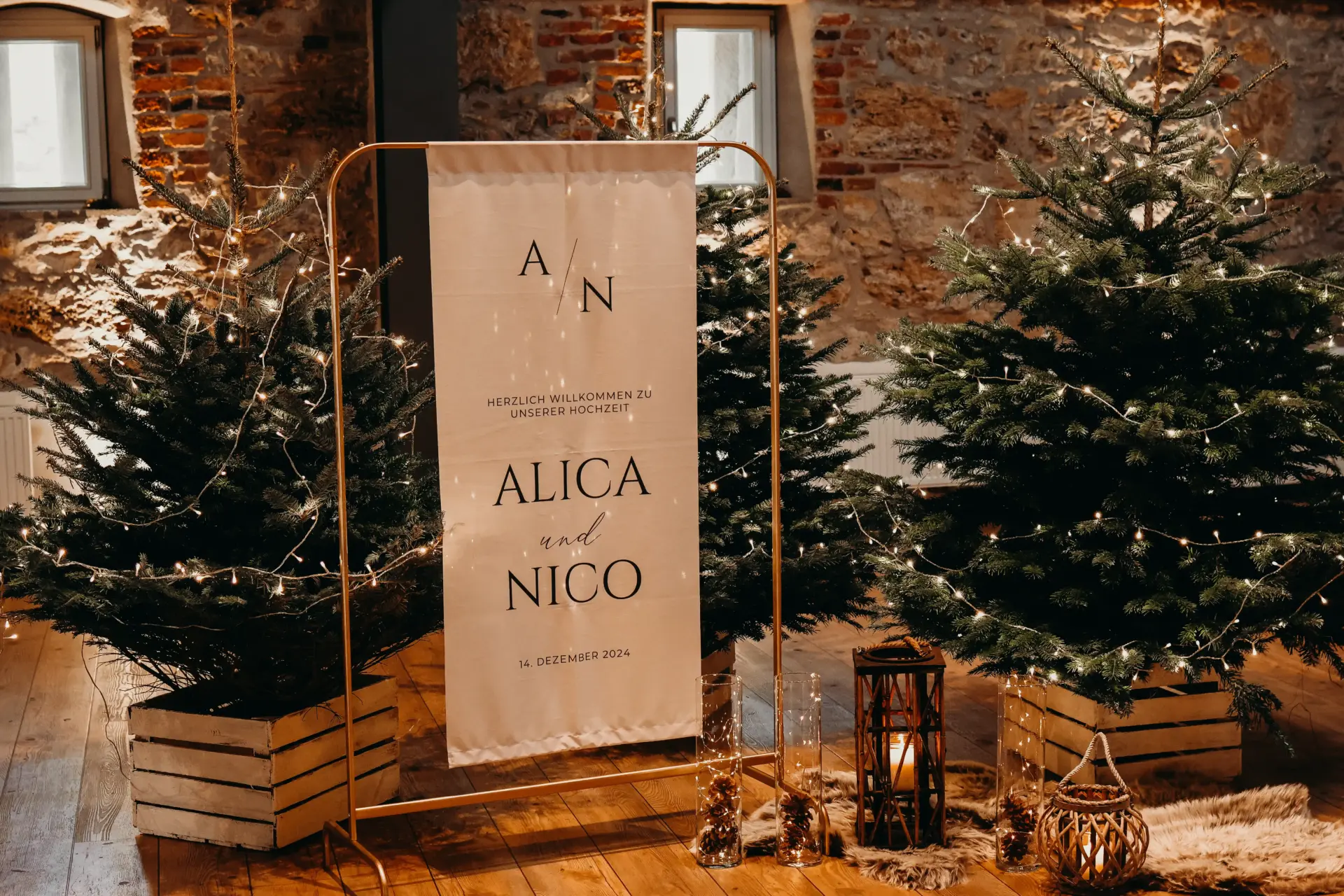 Willkommes-Dekoration einer Winterhochzeit in Form eines Stoffbanners mit Aufdruck, sowie 3 Tannenbäumen mit Lichterketten.