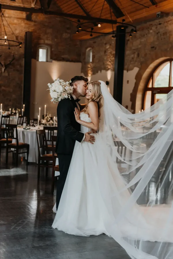Brautpaar in der Eventscheune in weißem Kleid mit langem Schleier und im schwarzen Anzug.